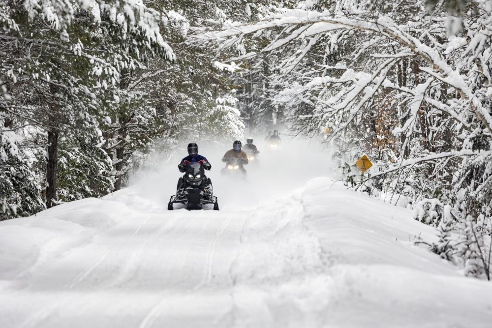 Snowmobile the Adirondack Rail Trail Snowmobiles ride in a line on a snowy trail