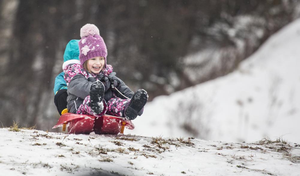 Two small kids smile as they slide down a hill on a plastic sled