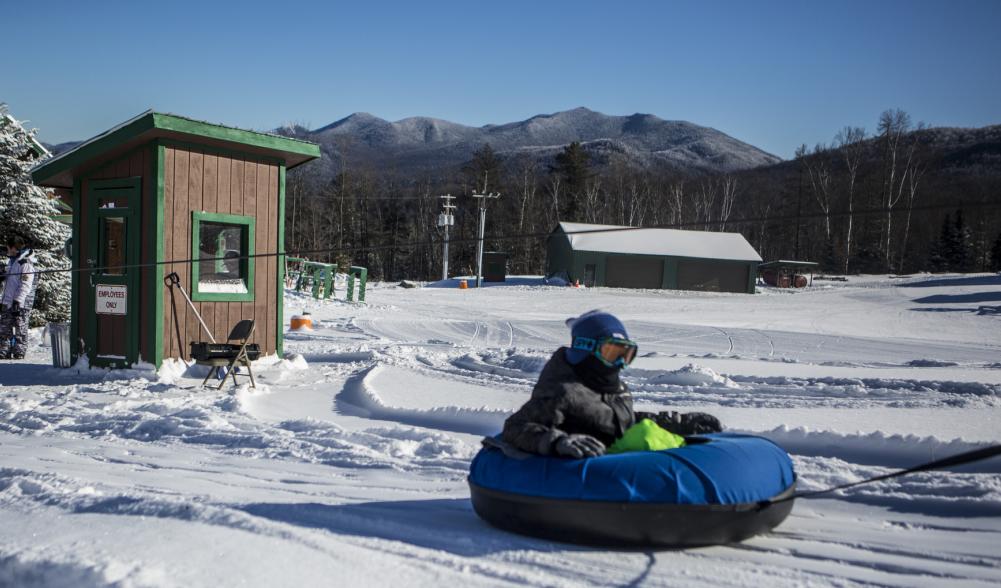 A child sits in a snow tube that is being pulled to the top of a sledding hill by tow rope