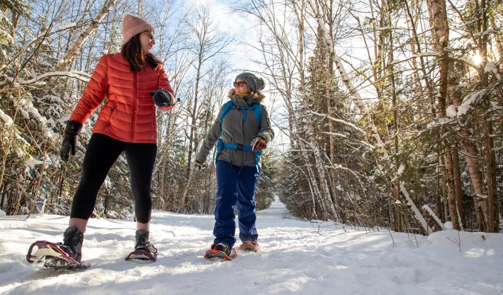 Two females chat as they snowshoe through the snow covered trees in Lake Placid