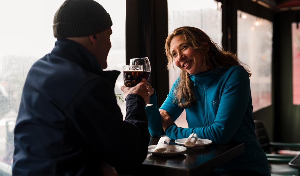 A man and woman cheers wine at a window-side table.