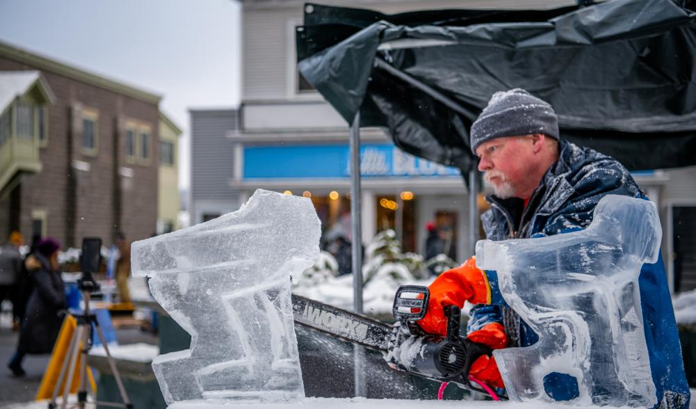 A man holding a chainsaw carves a sculpture out of ice.