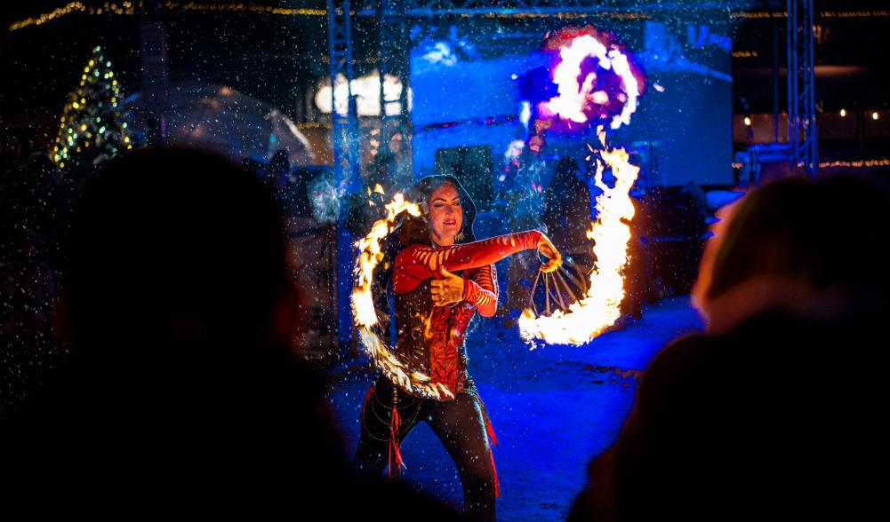 A dancer twirls flaming sticks in front of a crowd at night.