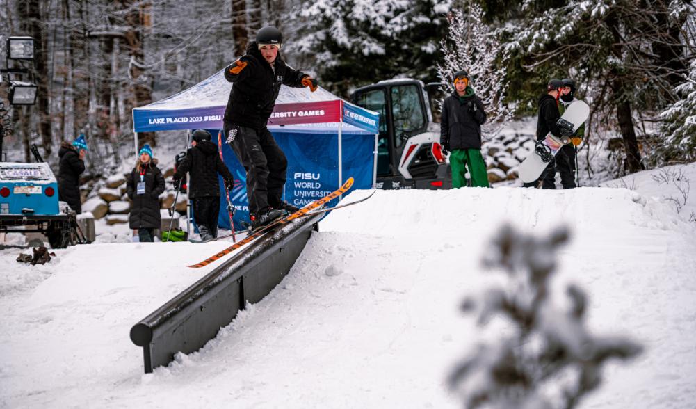 A snowboarder rides down a railing on a snowy bank.