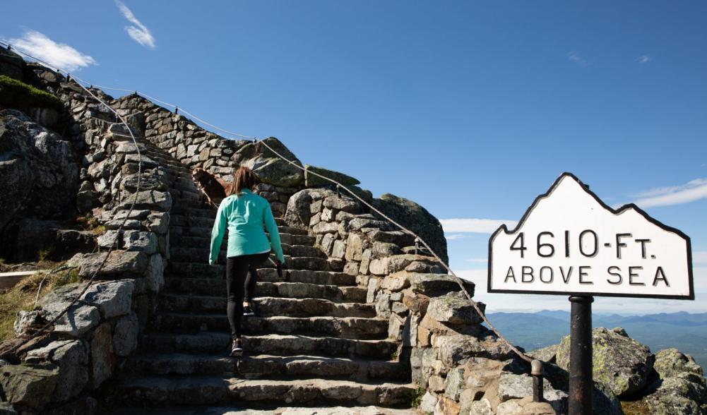 Visitors ascend the stairs towards Whiteface castle on the summit with mountains in the background.