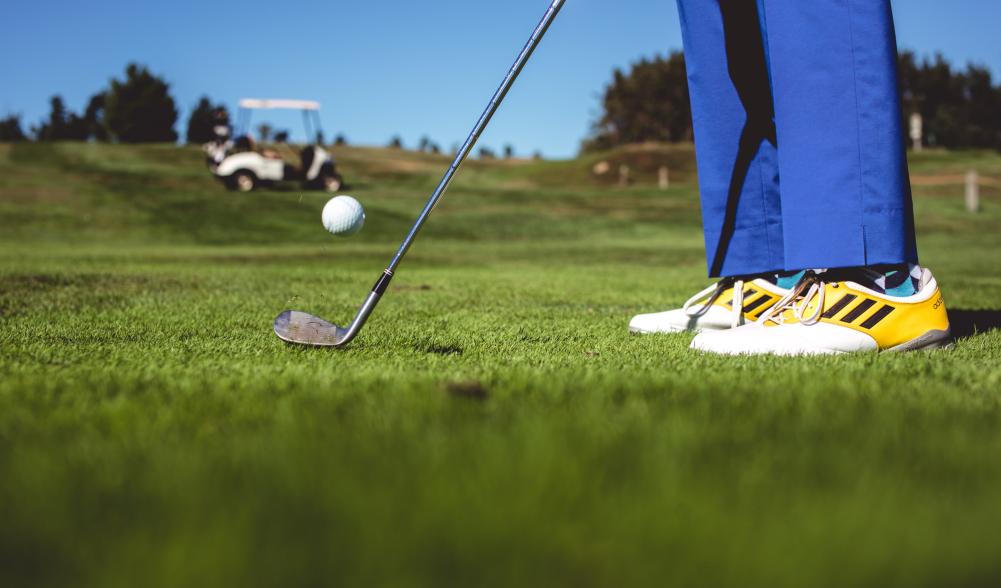 Close-up of a golfer's feet as he strikes the ball with cart in background.