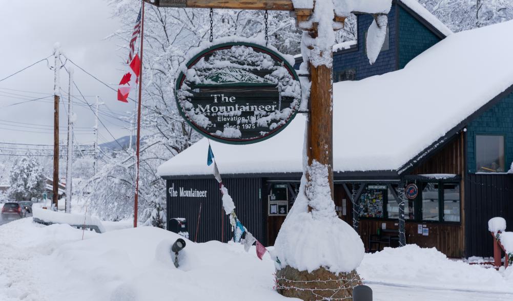 The Mountaineer's ice axe sign covered in snow, in front of the main shop building
