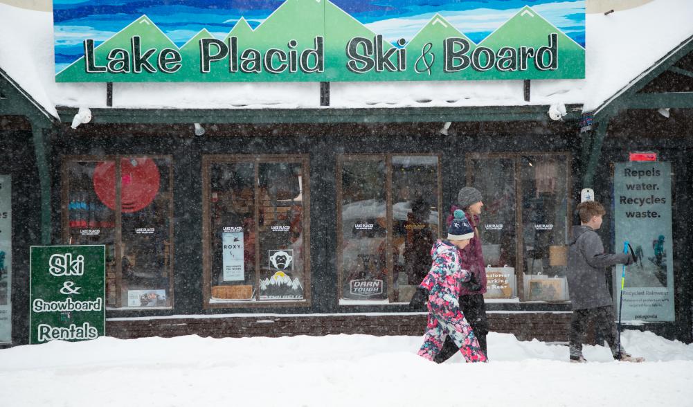 Snow is falling as a family walks by Lake Placid Ski and Board