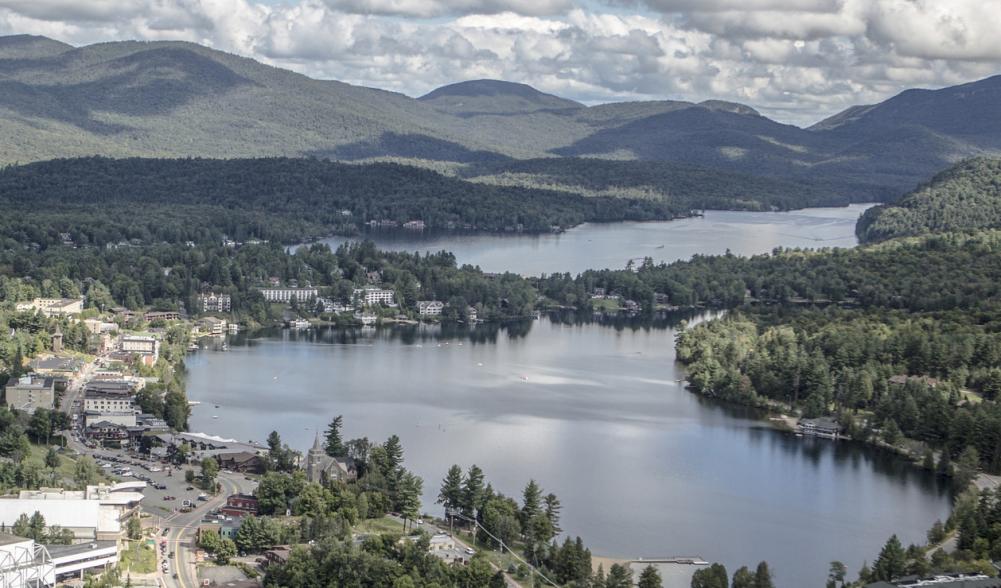 An aerial view of the village of Lake Placid, lined with shops and restaurants, and adjacent to Lake Placid lake and Mirror Lake.