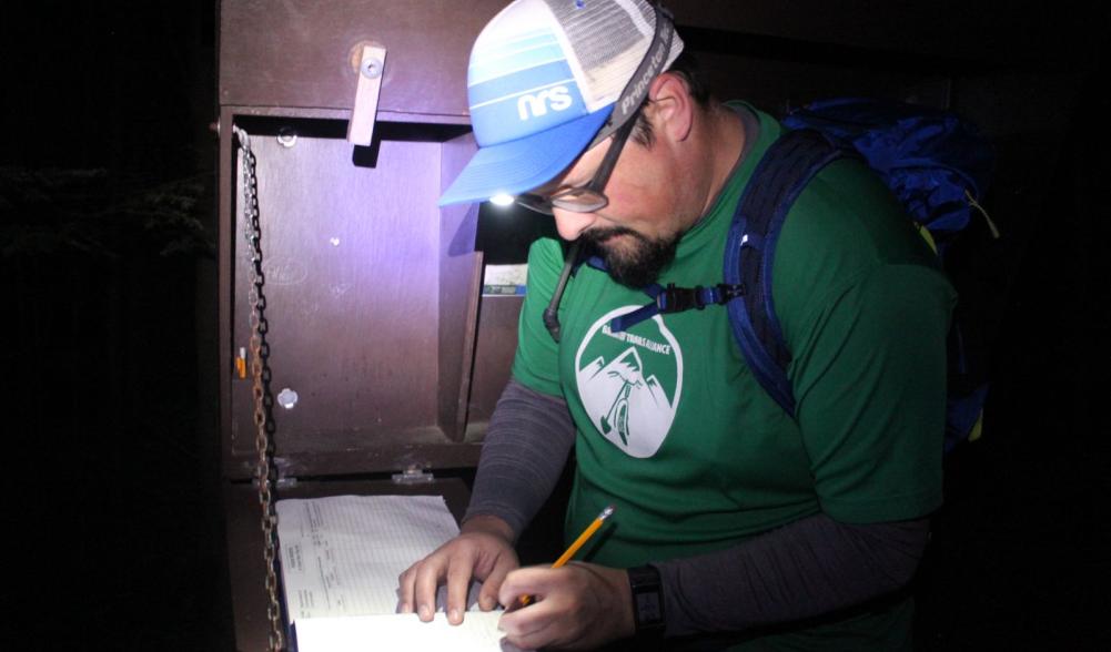 Dan signs the trail register by the light of his headlamp.