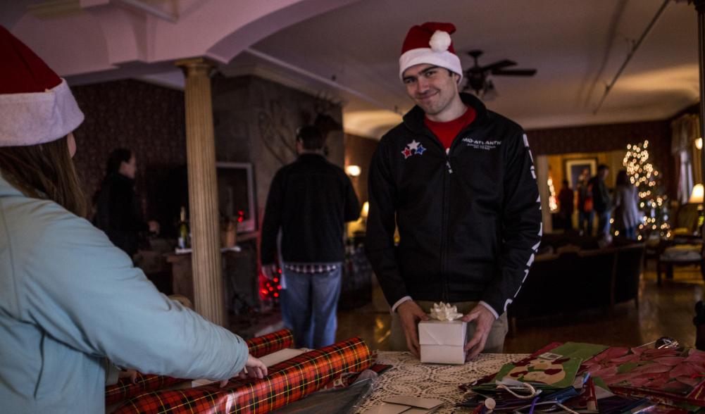 A man in a Santa hat poses at a gift wrapping table.