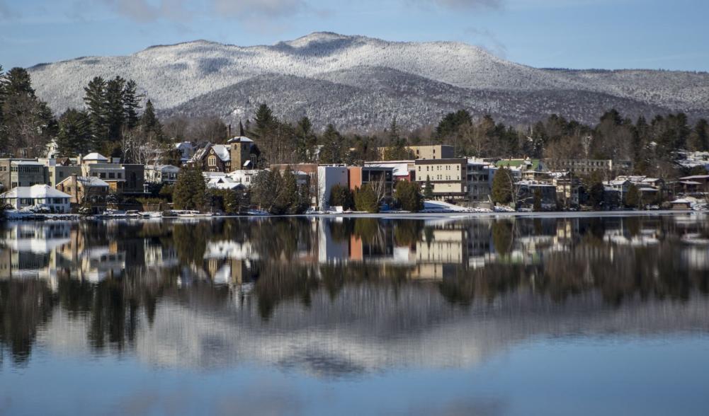 A view across a lake at a snowy village with mountains beyond.