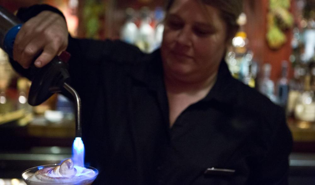 A bartender uses a small torch to brulee a cocktail.