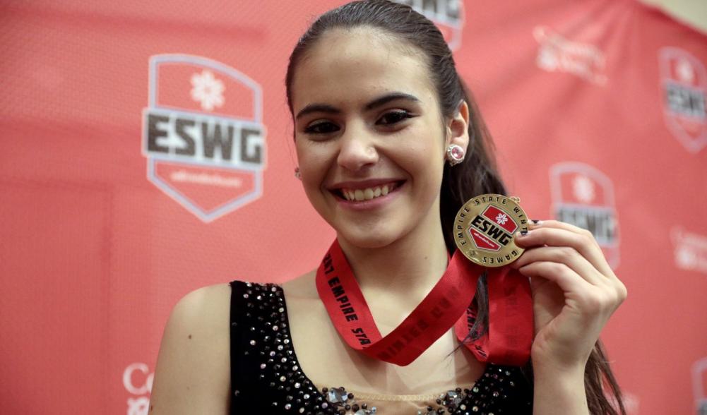 A teenage figure skater smiles and holds up her Empire State Winter Games medal.