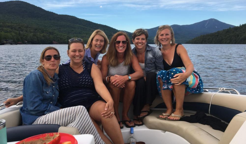 Six women on the front of a boat on one of Lake Placid's boat tours with mountains in the background
