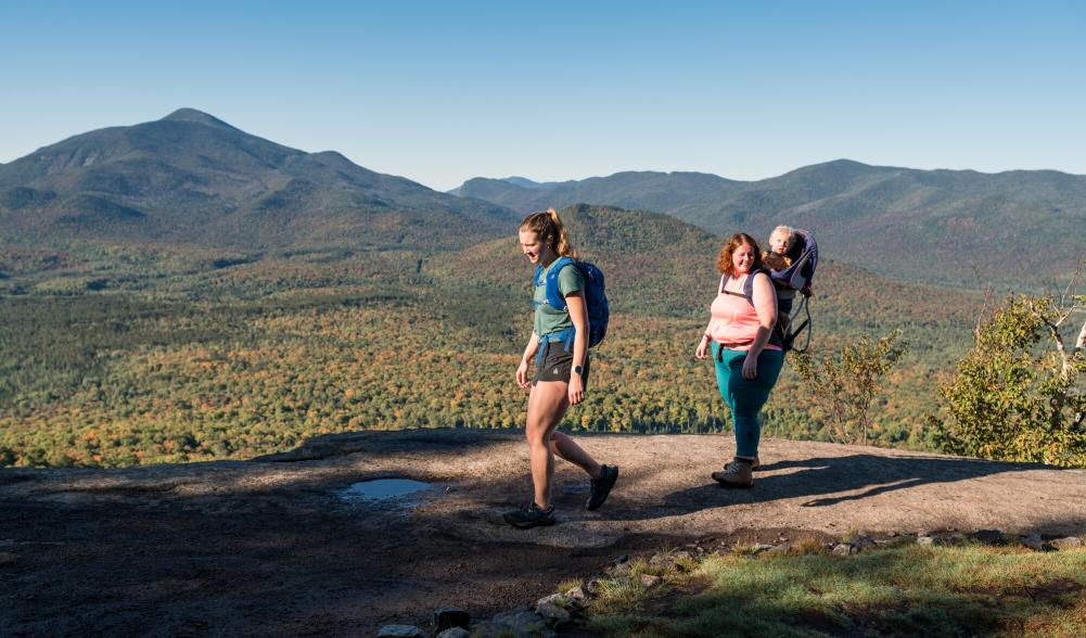 Two women and a baby at the summit of Mt. Van Hoevenberg in early fall overlooking the mountain range.