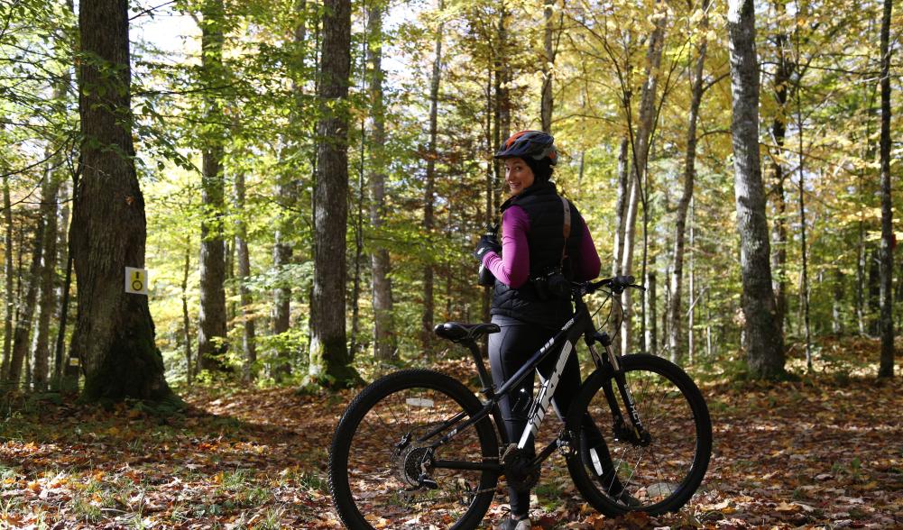 "Female smiling at the camera with a Lake Placid mountain bike rental surrounded by fallen leaves