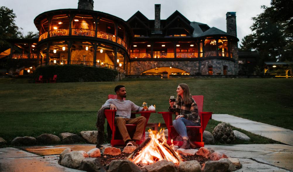 A man and woman enjoy a glass of wine at a fire pit on resort property.