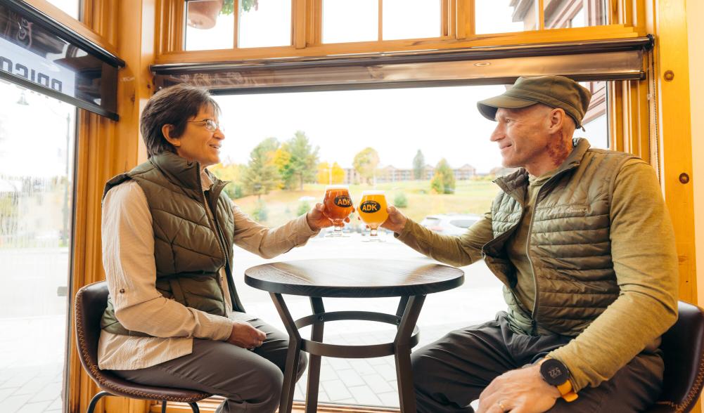 A man and woman cheers beers together at a brewery.