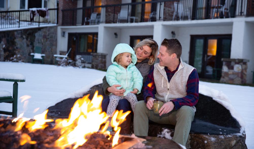 A couple with their child in front of a fire outdoors.