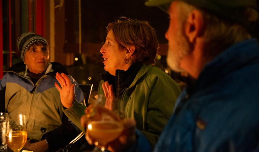 Two women and a man chat over a meal at an outdoor fire in winter.