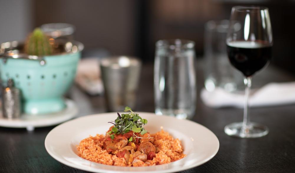 A plate of rice and jambalaya and glass of wine on a modern dining table.