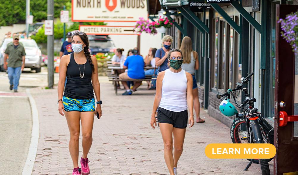 Two women stroll Main Street in masks and summer clothing.