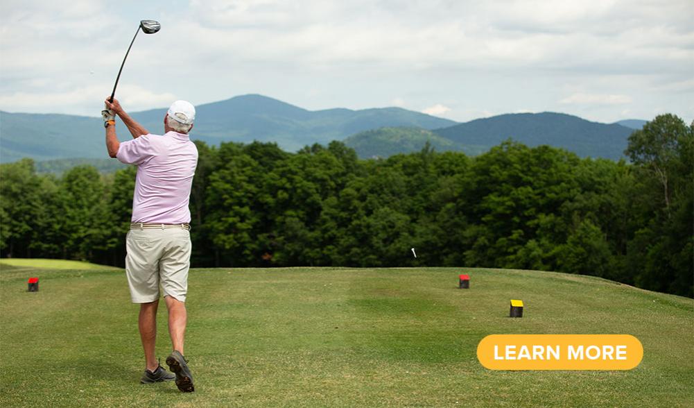 A golfer tees off toward the Adirondack Mountains.