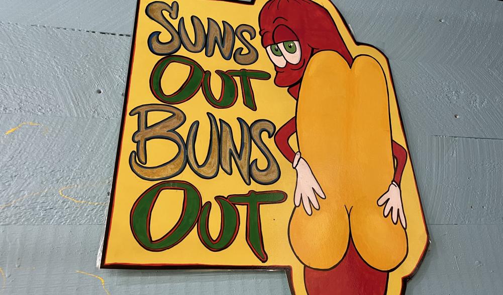 A vivid sign of a hot dog reads, "Sun's out, buns out!"