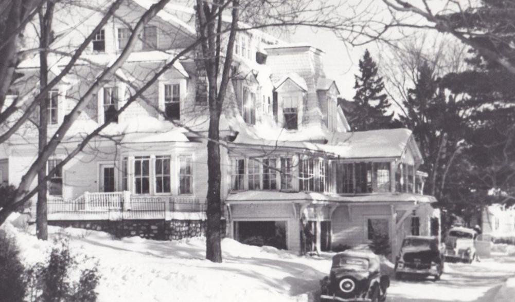 Vintage black and white photograph of the original Mirror Lake Inn, with early automobiles parked on the drive. Image courtesy Mirror Lake Inn.