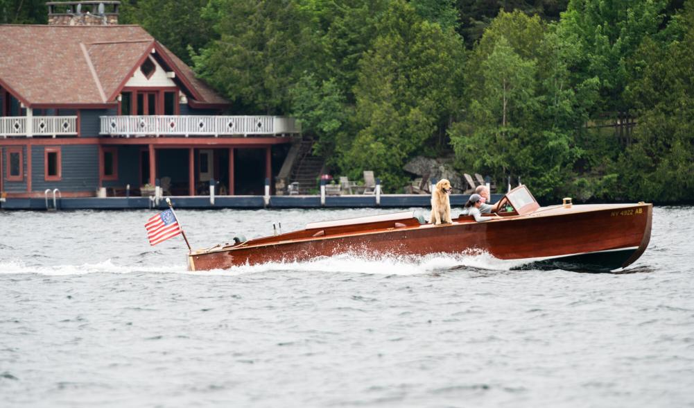 A sleek, classic wooden motor boat on Lake Placid lake with elaborate boathouse in the background.