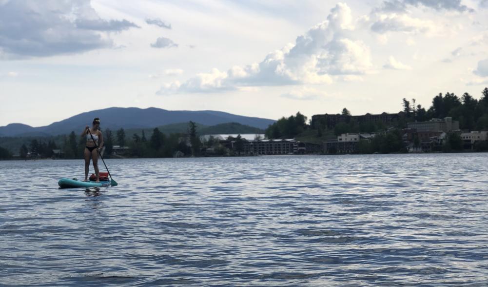 A woman paddles a SUP on a lake with mountains and trees in the background.