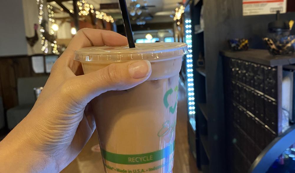 A womans hand holds up an iced coffee drink in a shop.