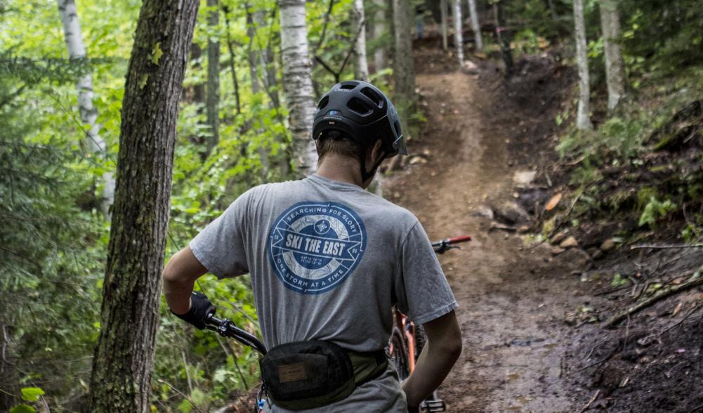 A mountain biker prepares to head up a wooded trail.