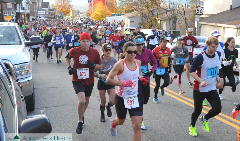 Runners race down a road aligned with fall foliage.