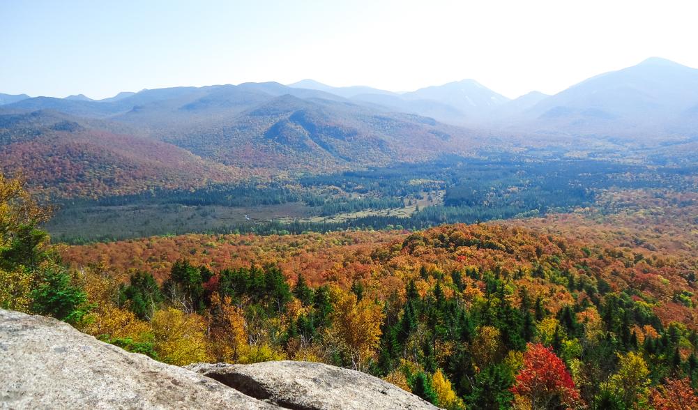 Fall view from the summit of Mount Van Hoevenberg. The High Peaks are covered in vibrant, colorful foliage.