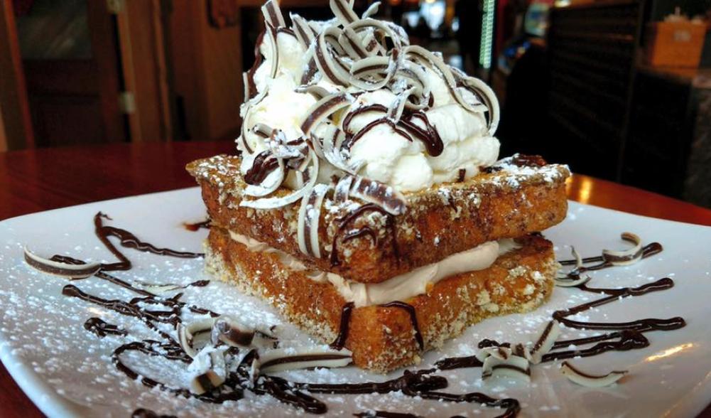 Two pieces of French toast with creamy filling and topped with a big mound of frosting and chocolate curls.