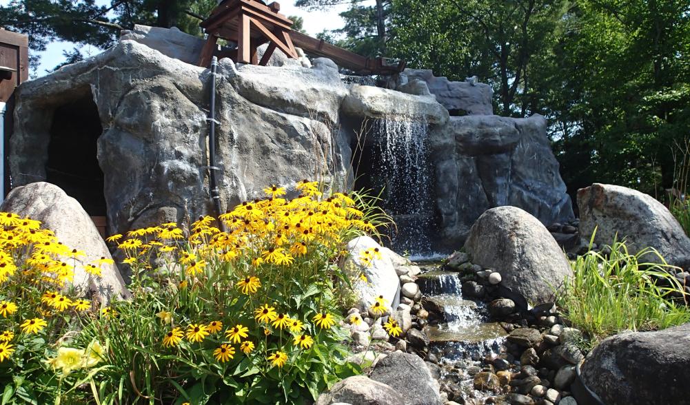 Black-eyed susan flowers in front of a rocky waterfall feature on a mini golf course.