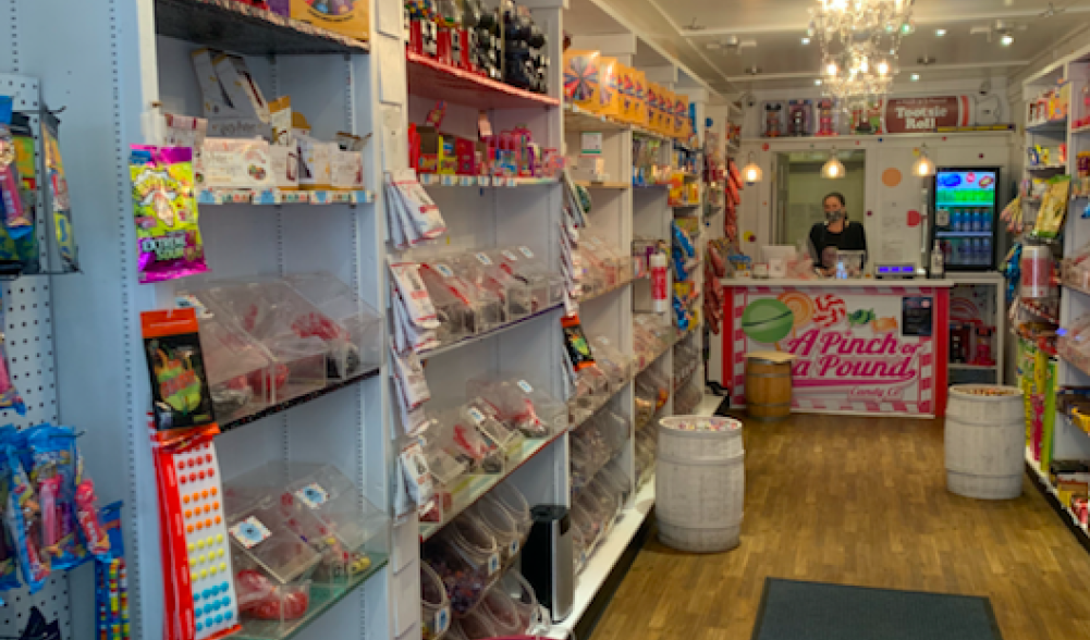 A white shop with chandeliers and shelves filled with brightly colored candy.