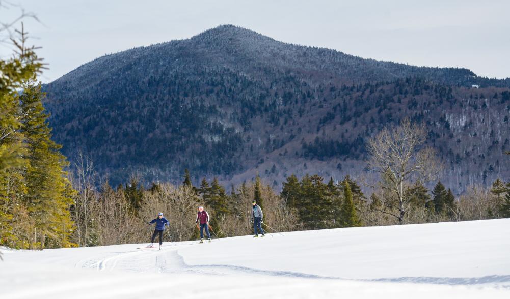 Cross-country skiers glide across snow with an Adirondack peak behind them.