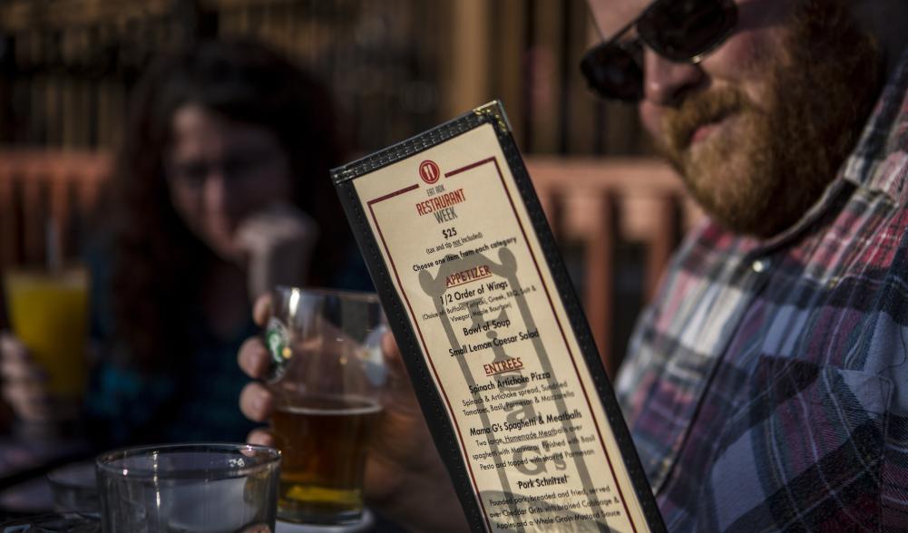 Man looks at menu with drink in his other hand