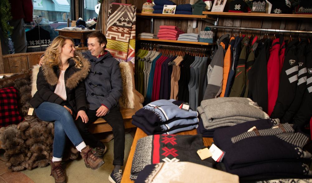 A smiling couple sitting down while shopping in a clothing store.