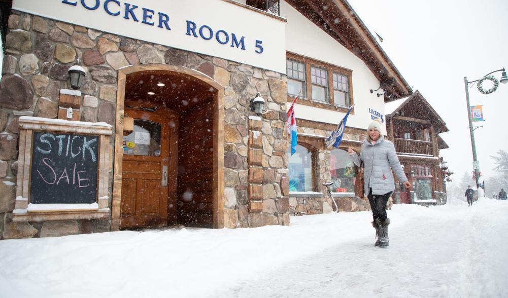 As the snow flies, a woman in a white coat walks by Locker Room 5.