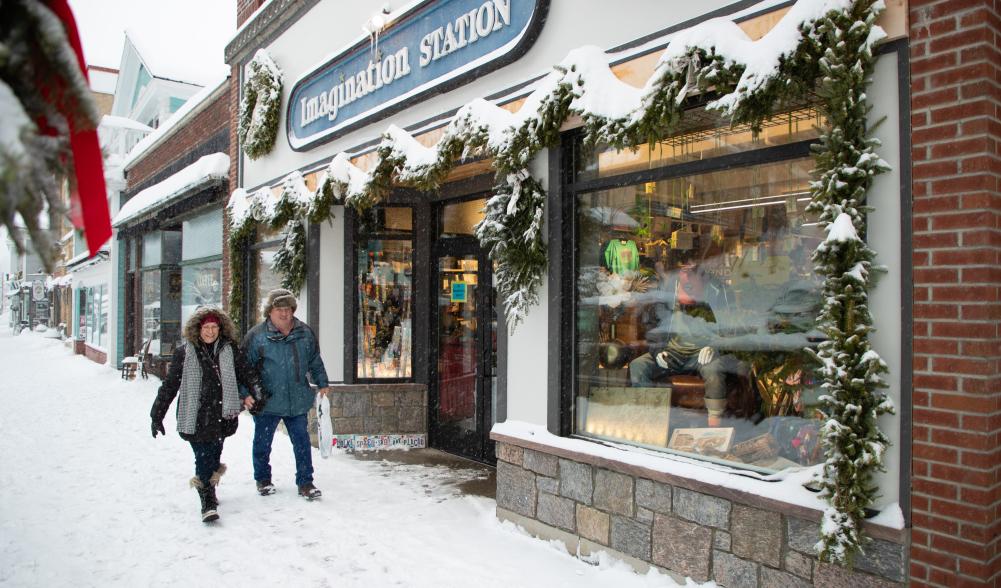 A man and woman walking together down a snowy Main Street sidewalk.