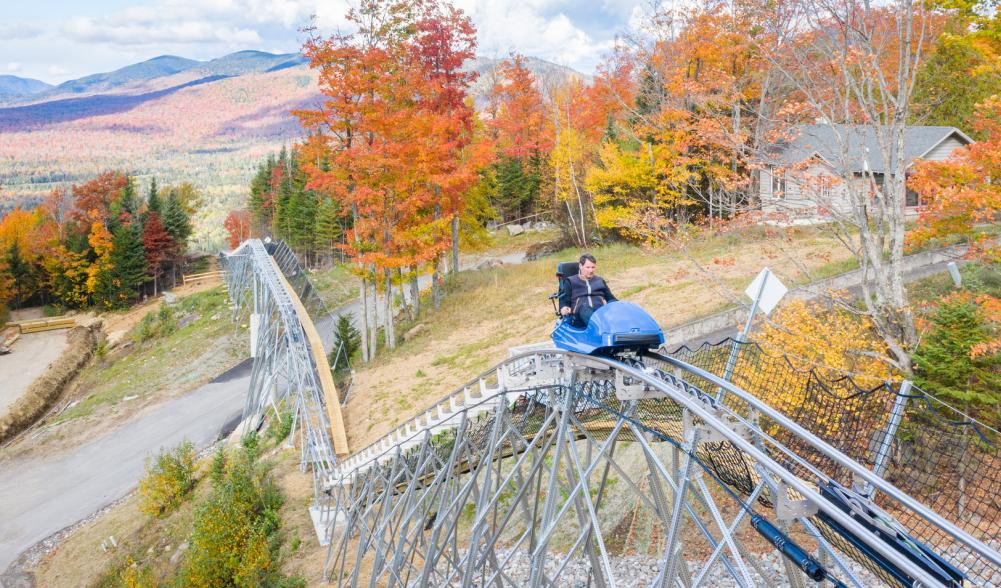 Man rides mountain roller coaster with fall foliage and mountains in background