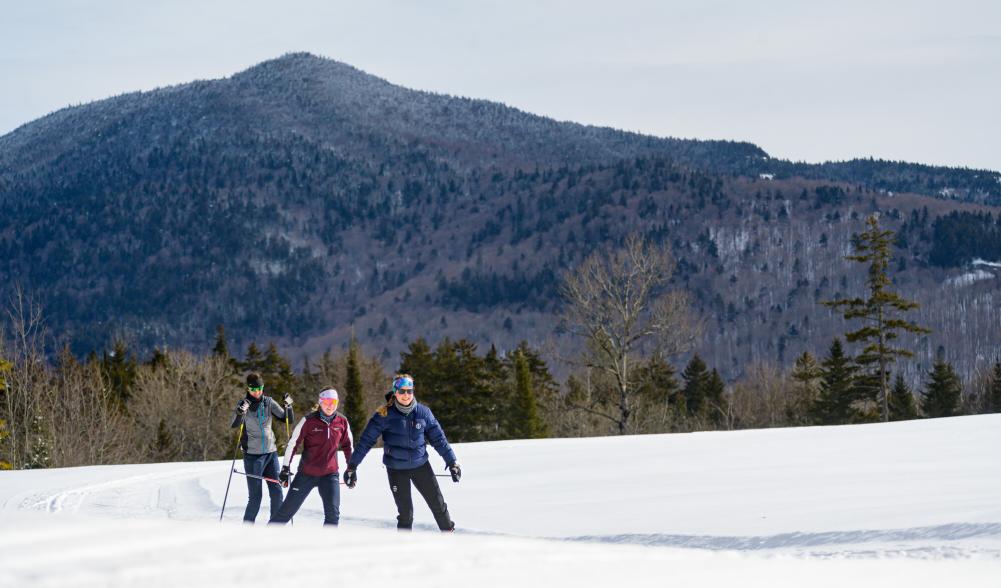 Three people cross country ski with mountain in background