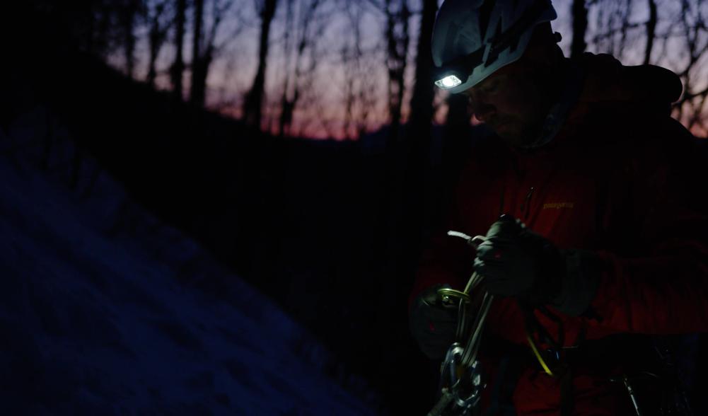 Man stands organizing ice climbing gear at dawn