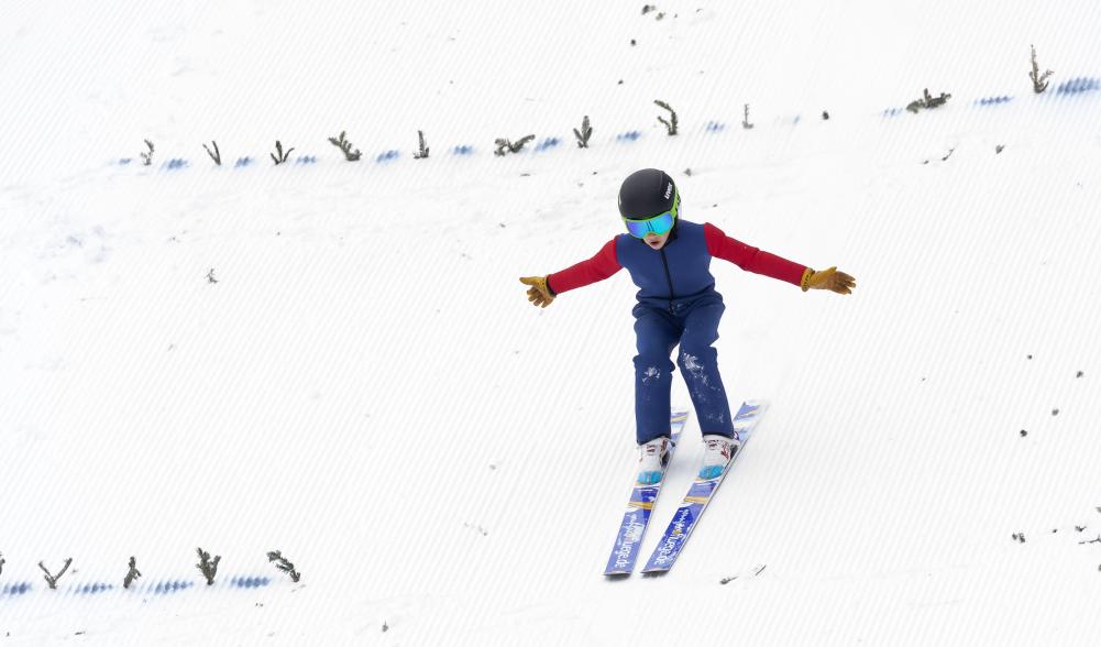 A young ski jumper landing on the snow.