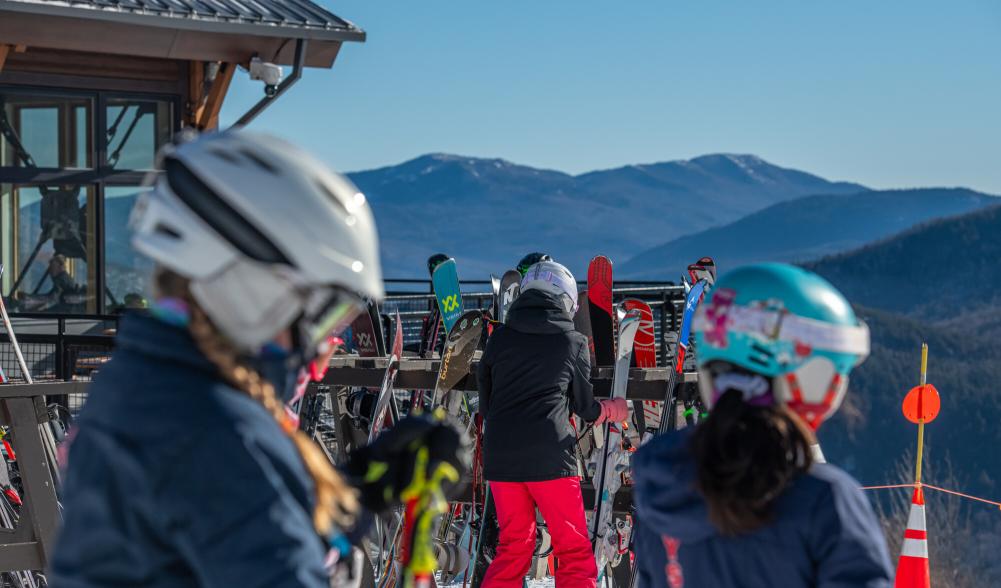 Skiers retrieve their skis from the stands outside a building.