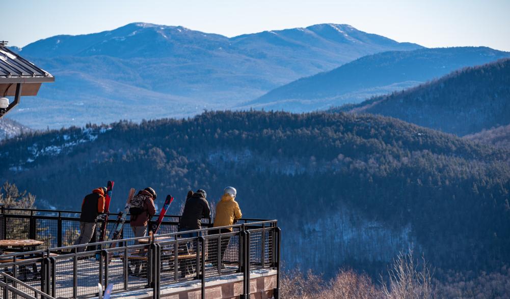 Four friends stand on a patio and look at the winter mountain views across the valley.
